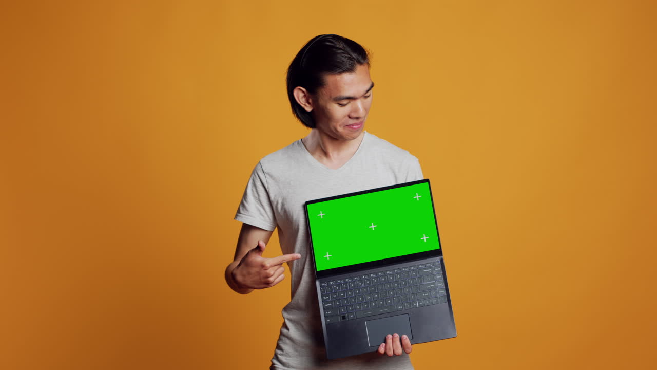 Cheerful man holding laptop with greenscreen on camera
