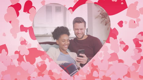 animación de corazones sobre pareja diversa usando teléfono inteligente en el sofá