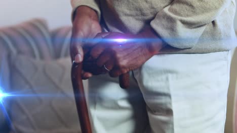 Animation-of-light-moving-over-senior-asian-man-at-home-on-couch-using-walking-stick