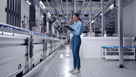 full body side view of asian female with her tablet with water production in bottling factory, she raises her fist up with screaming goal