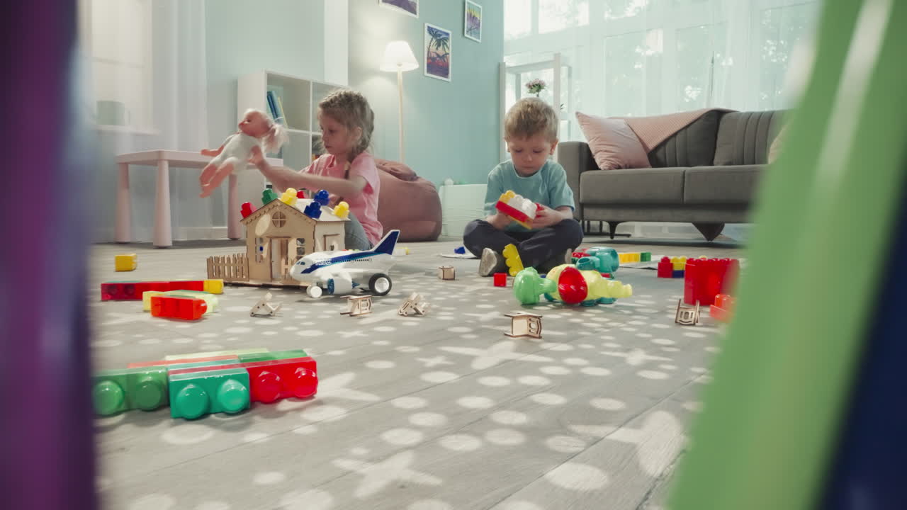 Toddler builds constructor while girl playing with baby doll