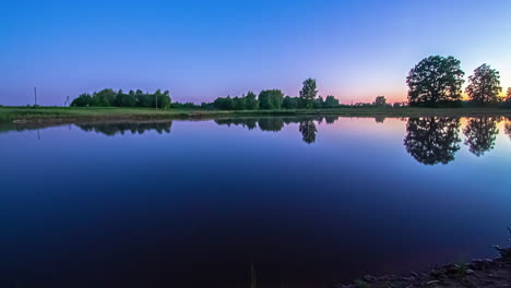 Friedlicher-Sonnenaufgang-Mit-Den-Farben-Des-Himmels,-Die-Von-Der-Glasigen-Oberfläche-Eines-Sees-Reflektiert-Werden---Zeitraffer