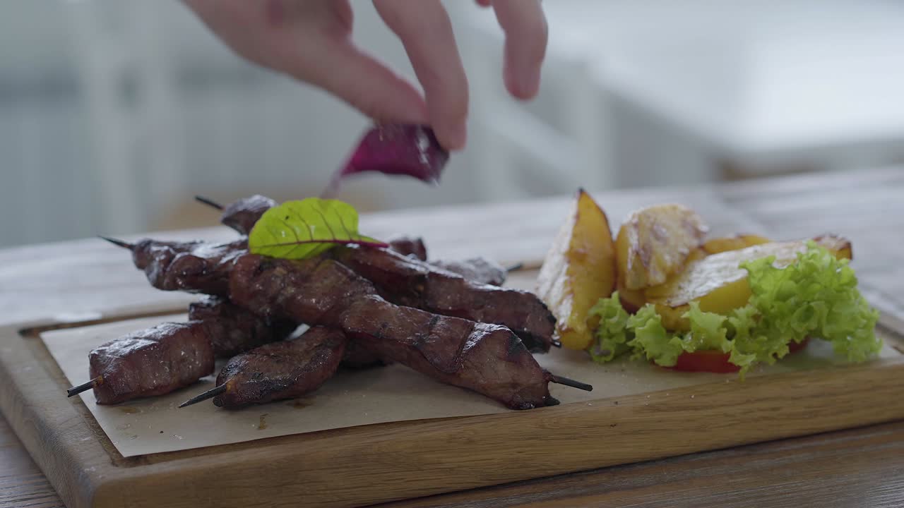 Chef che guarnisce con verdure un piatto splendidamente servito di verdure fresche, patate grosse e kebab, su pane pita