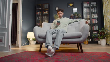 young man using smartphone while sitting on a couch at home 1