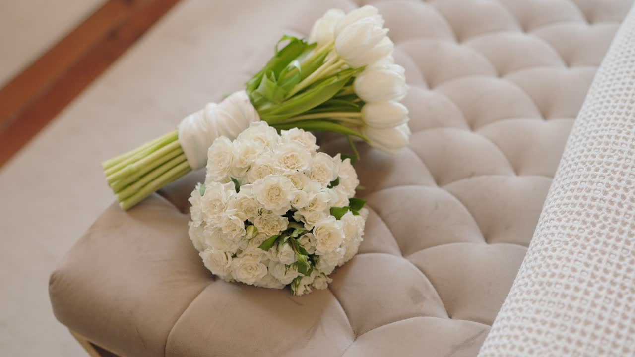 Two elegant white flower bouquets placed on tufted bench indoors