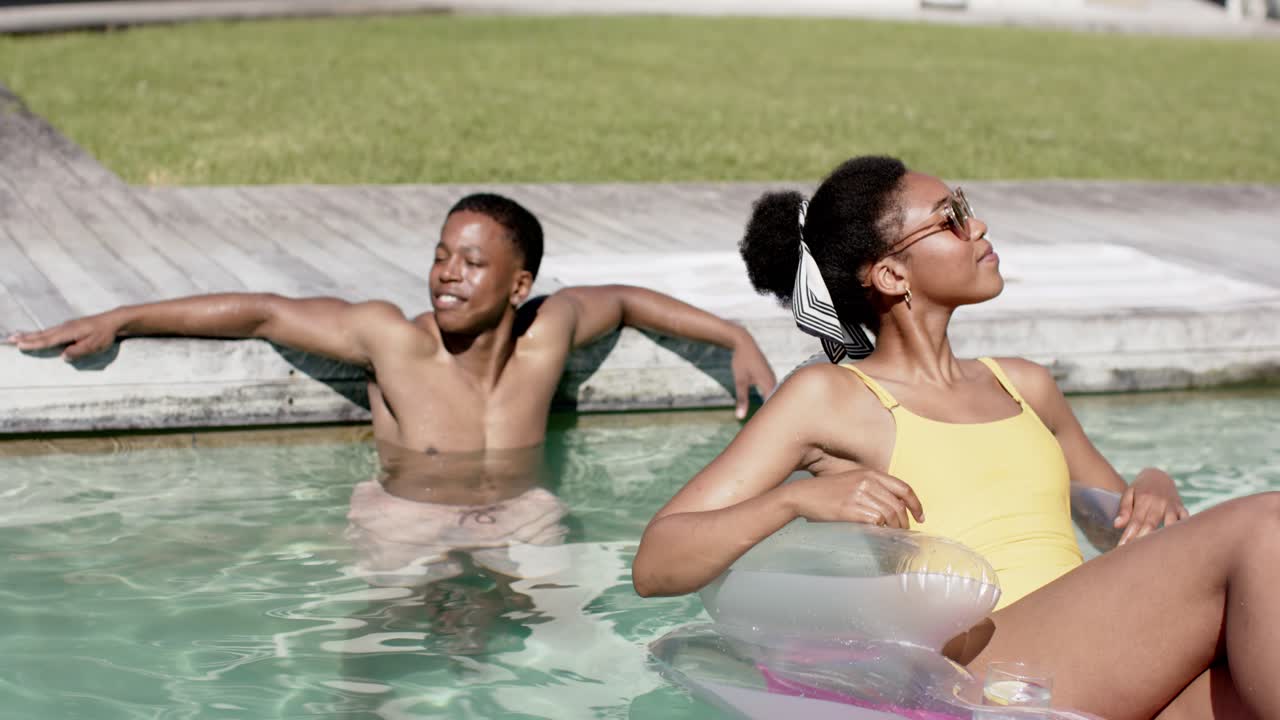 African American couple relaxing at pool sun making woman in yellow suit adjusting shades on float