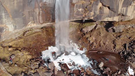 aerial flying back tilt shot of people walking near the frozen jogini waterfalls near manali, himachal pradesh during wintertime, shot with a drone in 4k