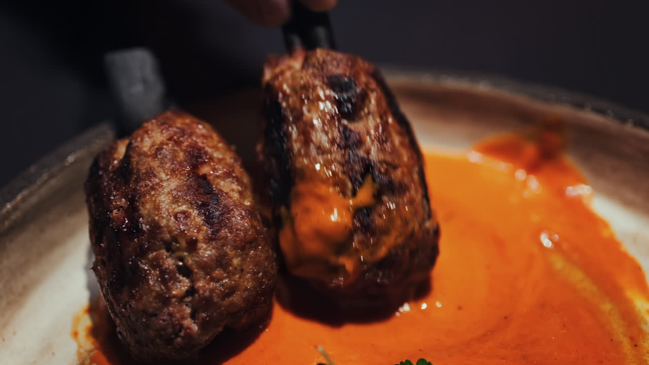 Two grilled meat skewers on charcoal sticks served on a plate with an orange sauce