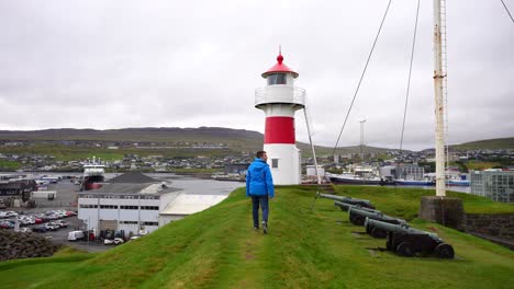 toma trasera de un hombre caminando hacia el faro en skansin en torshavn
