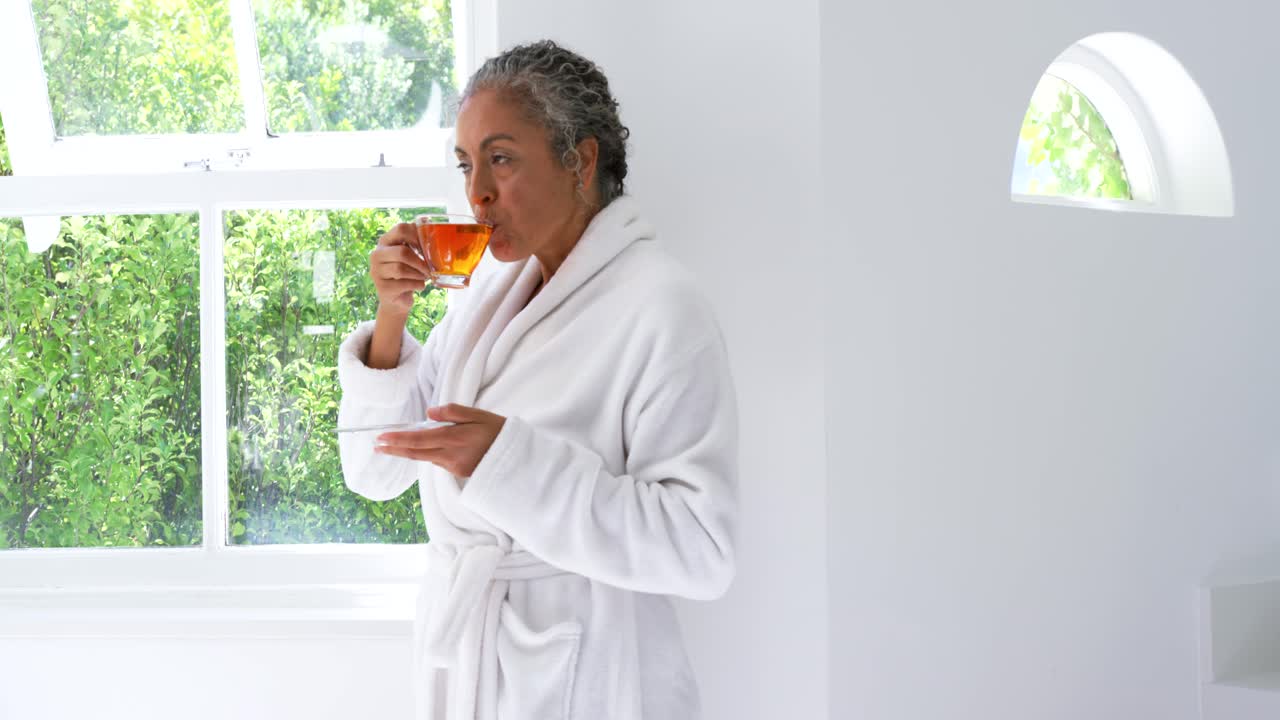 African American Senior woman in robe holding teacup by sunlit window sipping, savoring, copy space