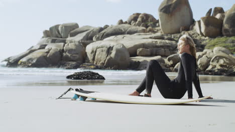 woman surfer relaxing on beach with surfboard