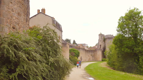 pan shot of tourists walking near the magnificent medieval castle wall in parthenay, france.