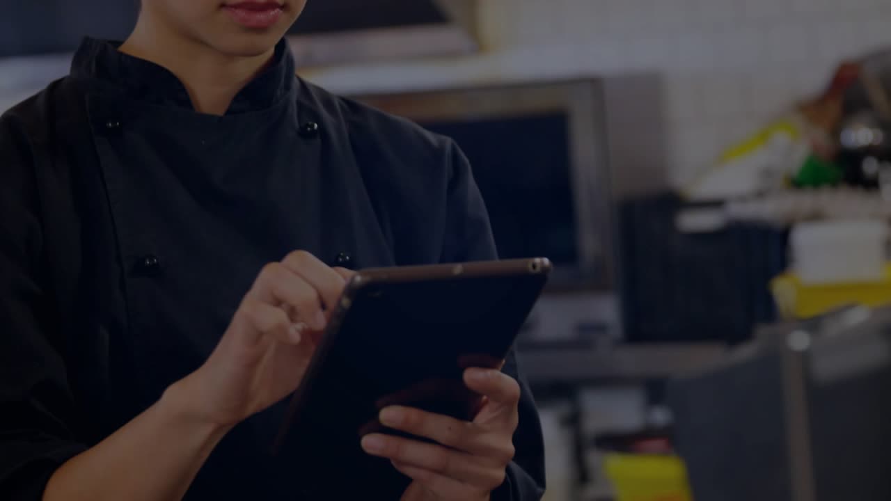 Female chef tapping tablet and reading in pro kitchen, initiating double-helix sweeping across face