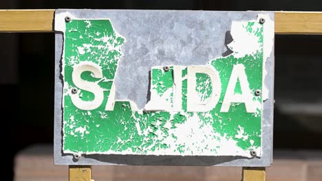 close-up of a weathered and peeling green sign with the word "salida" (exit) in spanish. a stark visual of urban decay on a street in madrid, spain