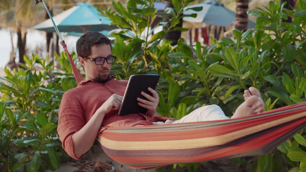 relajándose en una playa tropical en una hamaca con una tableta