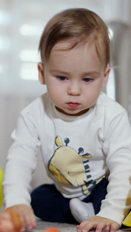 adorable little baby boy sitting among the bright toys indoors. toddler leaves his toys and crawls approaching camera. vertical video