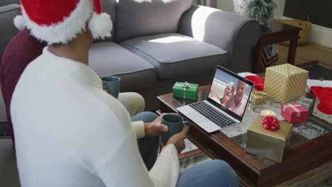 Padre-E-Hijo-Birraciales-Usando-Una-Computadora-Portátil-Para-Una-Videollamada-Navideña-Con-Una-Pareja-Feliz-En-La-Pantalla