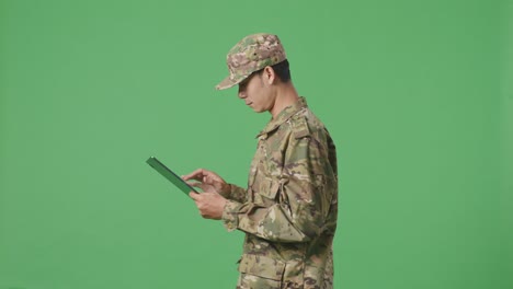 side view of asian man soldier using a tablet while walking in the green screen background studio