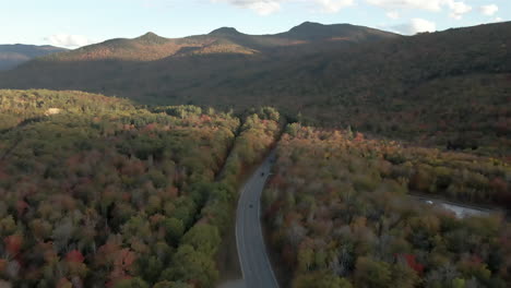 Aerial-forward-follow-cars-on-Kancamagus-highway,-mountains,-and-fall-foliage