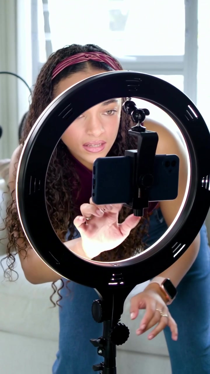 Vertical video: Entering studio woman in maroon top arranging phone, ringlight and mic to record
