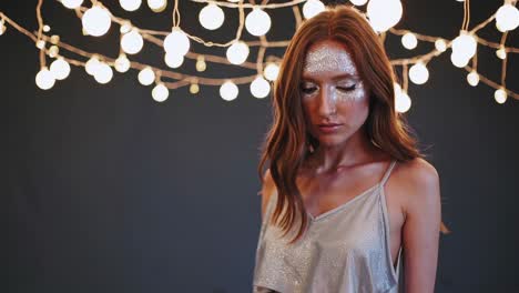 blurred fashion model posing gracefully under glowing string lights, showcasing striking silver makeup and a stylish two piece outfit in a serene studio with a dark backdrop