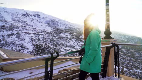 mujer con una chaqueta verde y un sombrero en un paisaje nevado en un día soleado y un reflejo del sol en la lente