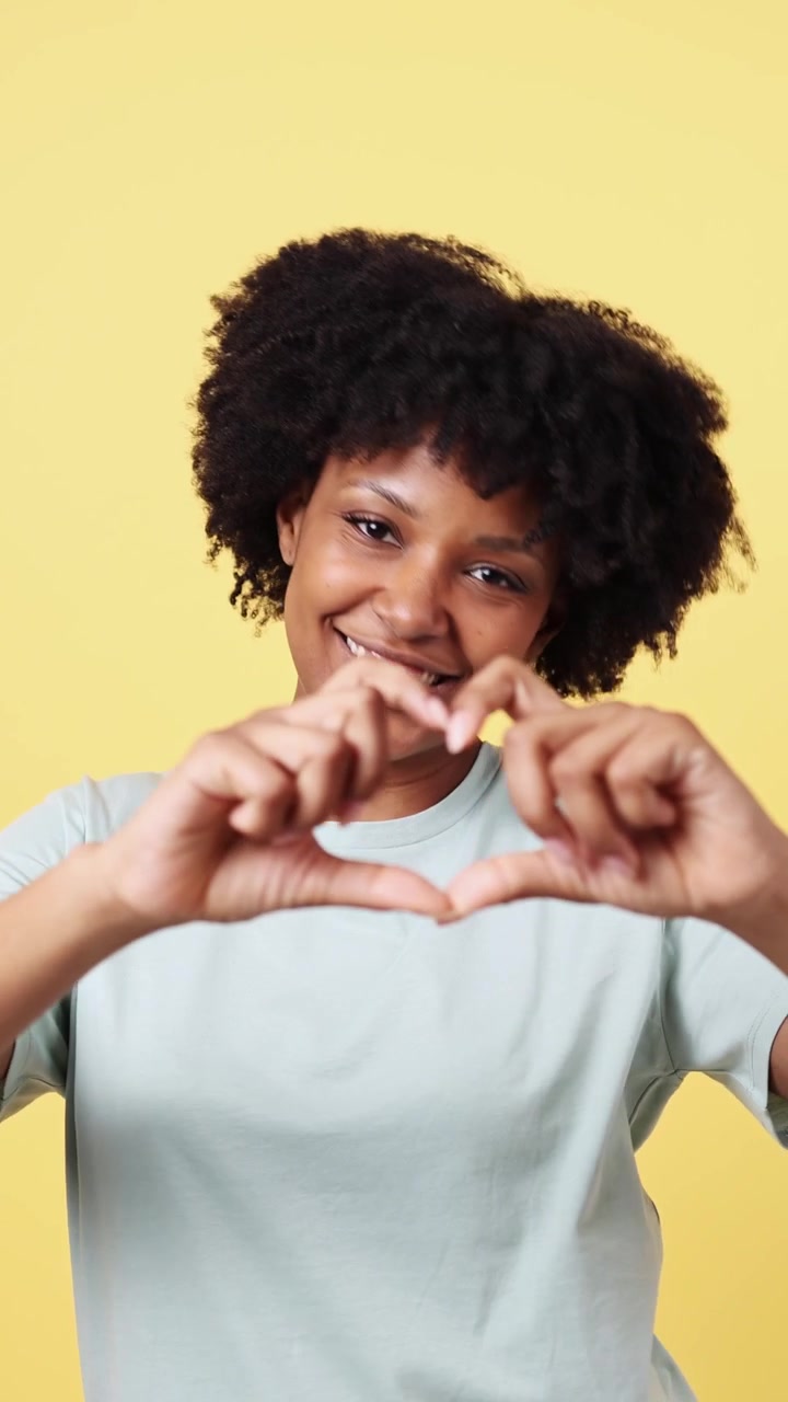 Giovane donna afroamericana che fa il gesto del cuore e sorride felicemente