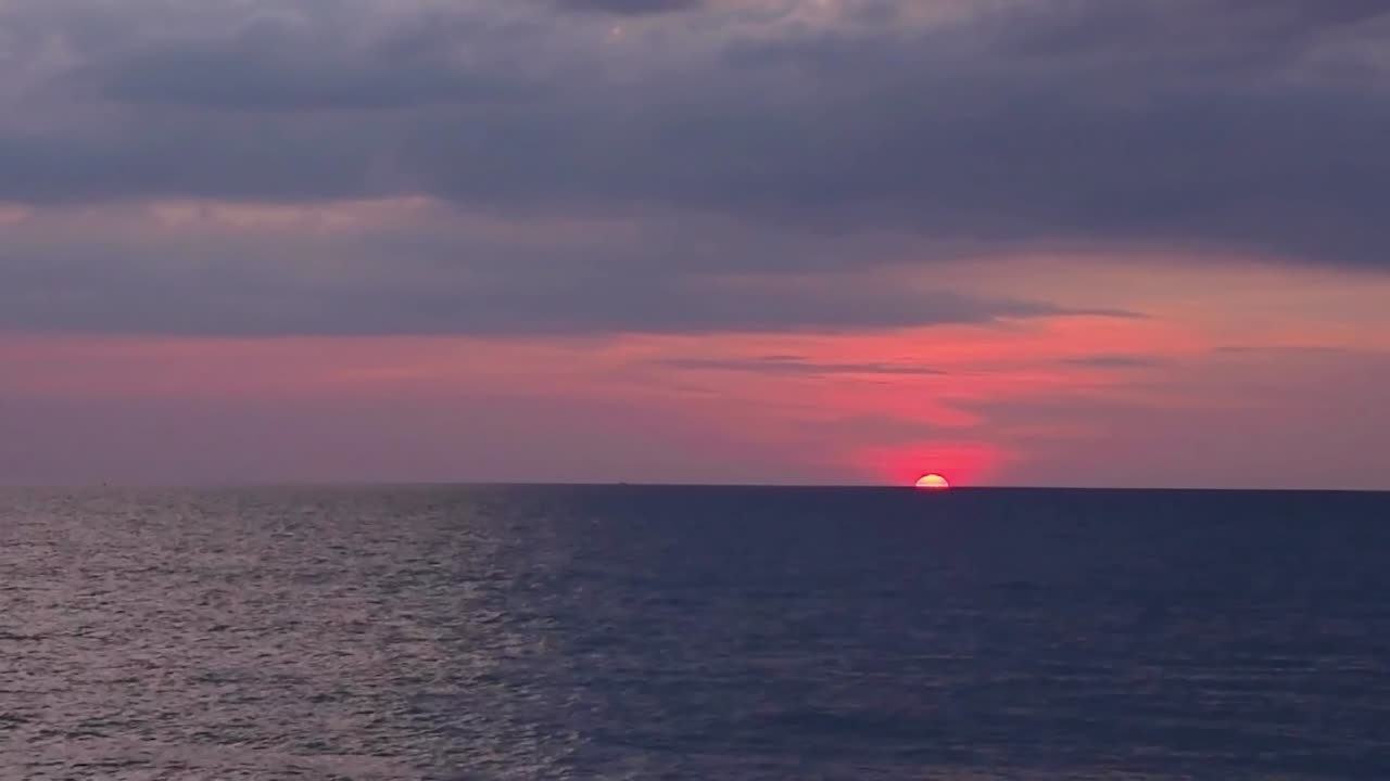 timelapse b-roll of sunset at the ocean. colorful pink red sky in rainy season. dark darmatic clouds moving slowly to the round red sun down into the sea. dron flying over sea sunset sceanary. nature
