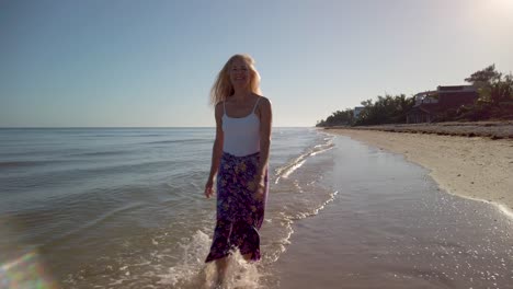 Mujer-Bonita-Y-Despreocupada-Con-Sarong-Y-Camiseta-Sin-Mangas-Salpicando-En-El-Agua-Caminando-Por-La-Playa-A-Cámara-Lenta