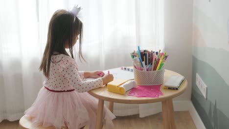 young girl sitting at a table, drawing with colorful crayons. ideal for themes of creativity, childhood development, learning, and art activities in a cozy indoor setting.