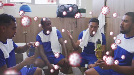 Covid-19-cells-floating-against-team-of-male-soccer-players-discussing-together-in-locker-room