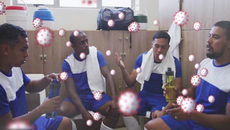 covid-19 cells floating against team of male soccer players discussing together in locker room