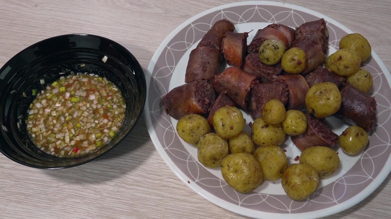 Fette di morcilla cotta e patate novelle condite servite su un piatto accanto a una ciotola di salsa aji tritata su un tavolo di legno