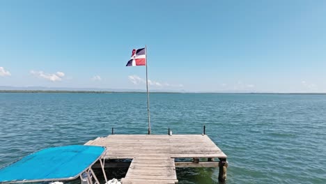 Aerial-forward-flight-over-wooden-jetty-towards-waving-flag-of-Dominican-Republic-at-Caribbean-Sea