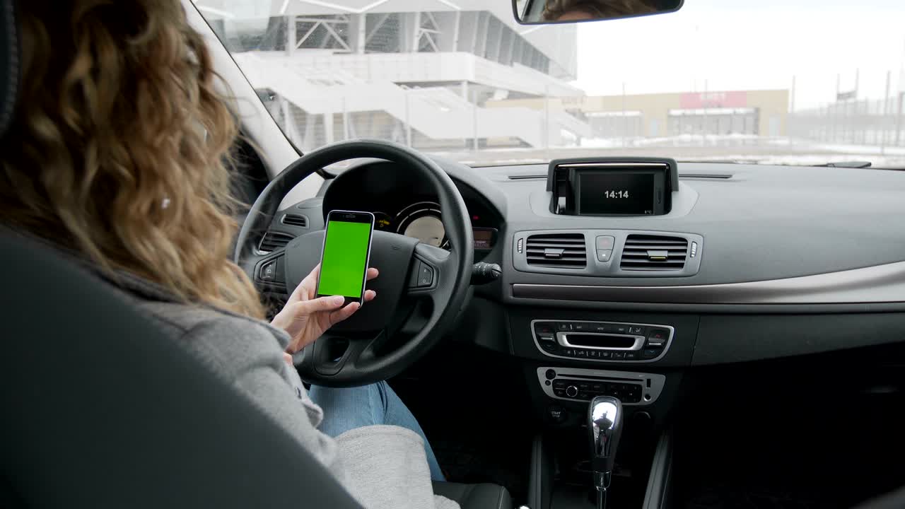 mujer se sienta en el coche moderno y trabaja en el teléfono inteligente - pantalla verde - primer plano