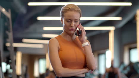 Curious-athlete-girl-using-phone-at-gym.-Sportswoman-standing-in-sport-club