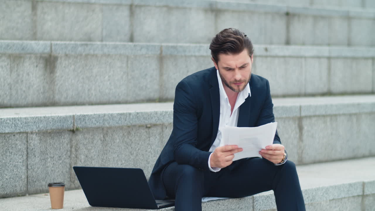 Businessman reading business papers on street. Man sitting on stairs