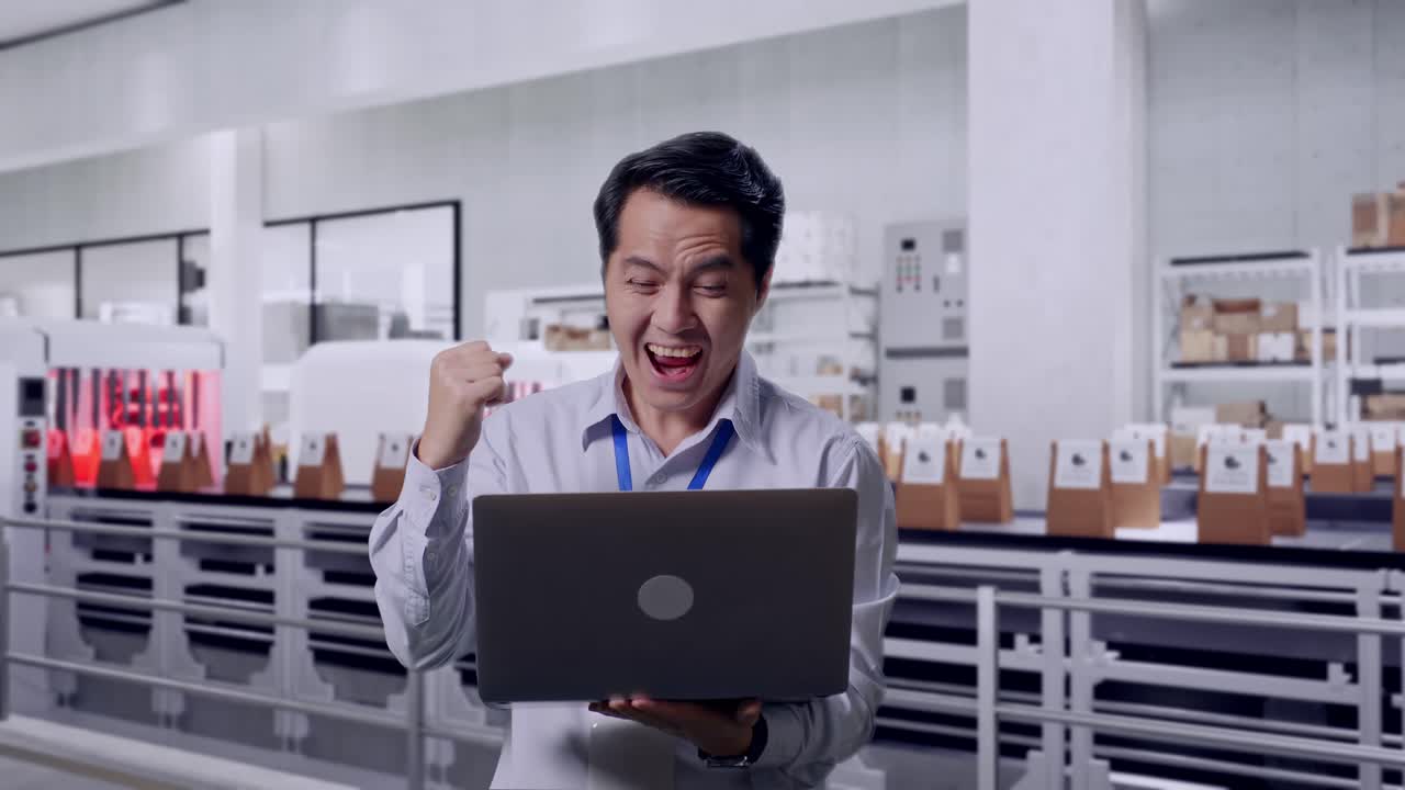 Asian Male Professional Worker Standing With His Laptop With Conveyor for Packaging Coffee Beans in Bags at Coffee Factory, He Raises His Fist Up With Screaming Goal