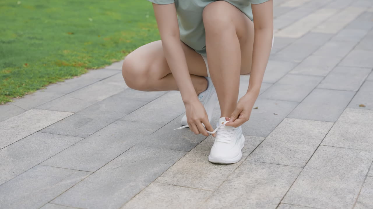 Atleta corredora atando o cadarço do sapato, pronta para treinar ao ar livre no parque. Captura da preparação e determinação para uma sessão de fitness ao ar livre.