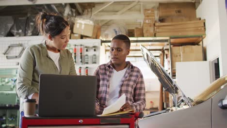 Video-of-two-diverse-female-car-mechanics-using-laptop-and-smartphone,-searching-for-car-parts