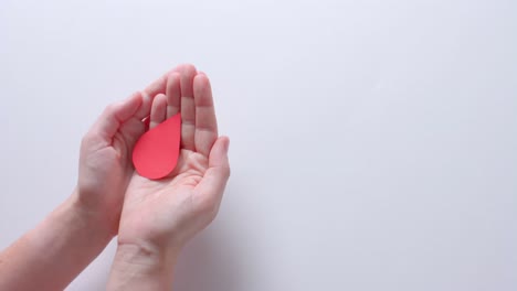 hands of caucasian woman cupping blood drop on white background with copy space, slow motion