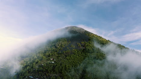 retiro aéreo de las laderas de suelo de basalto con bosque verde exuberante mientras las nubes rodan a través del cono