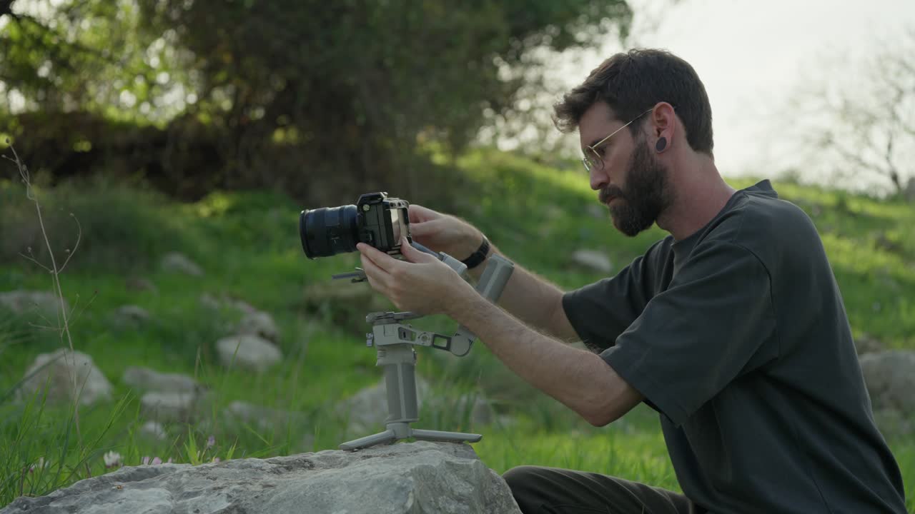 Videographer balancing camera gimbal on a rock while preparing for filming outdoors