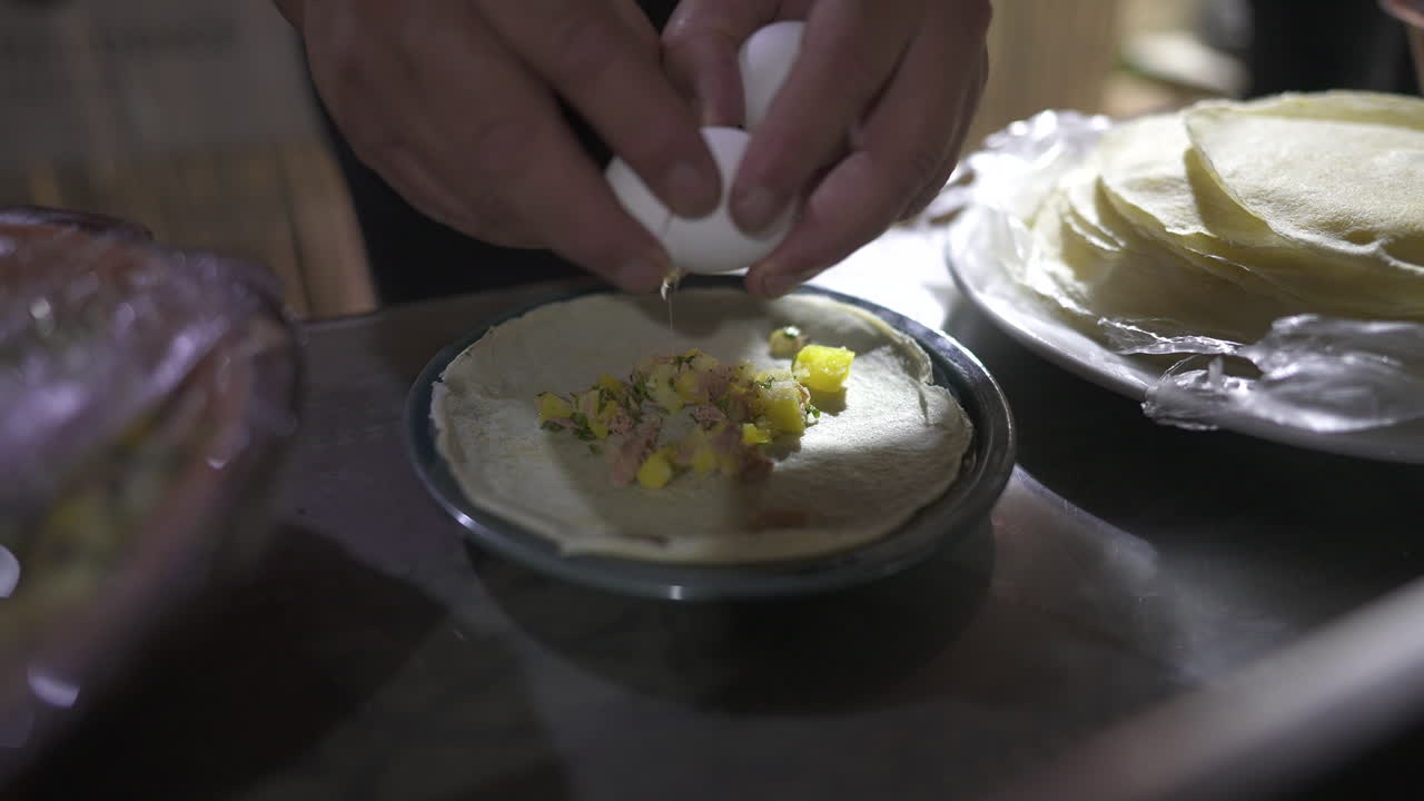 Mani che rompono un uovo fresco su una piadina mentre preparano un semplice pasto fatto in casa sul ripiano della cucina