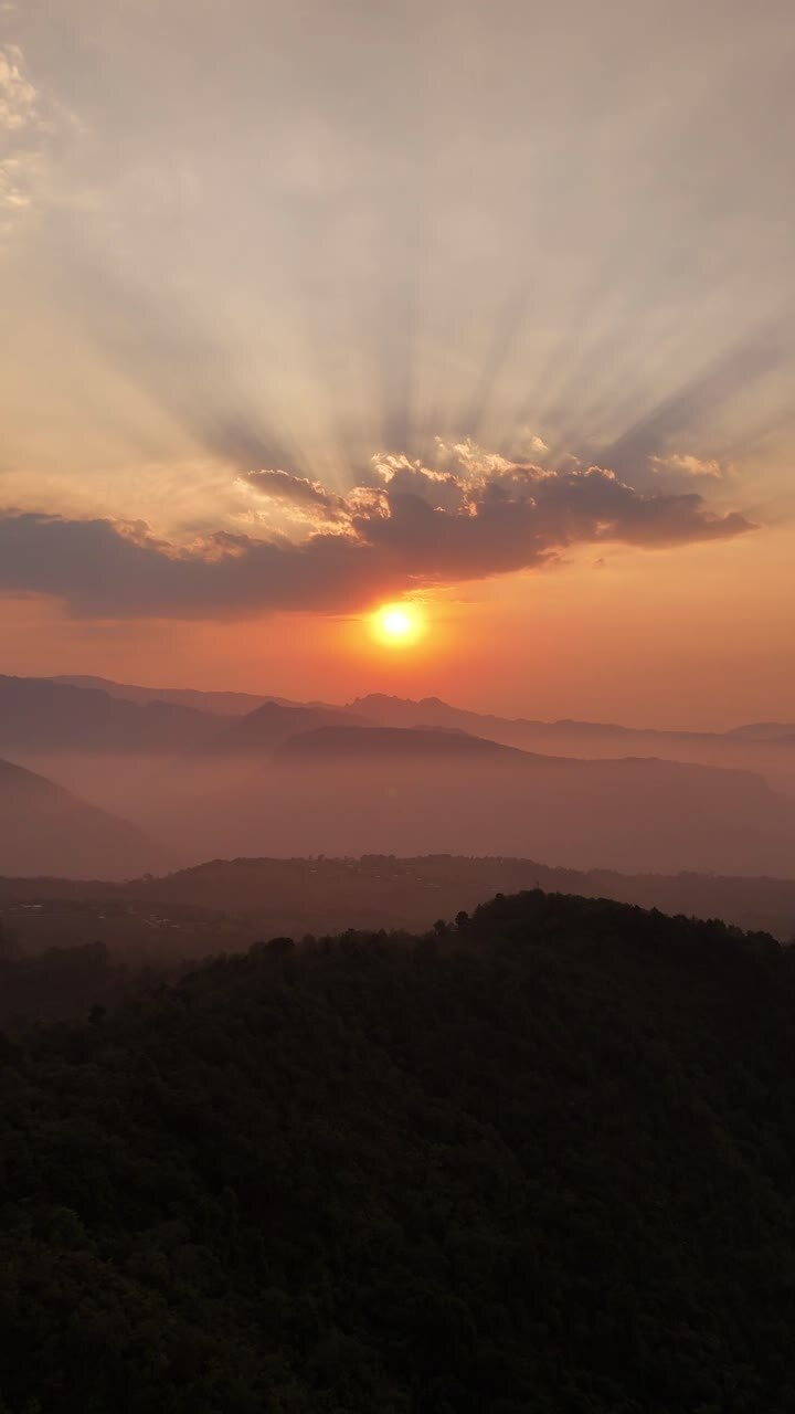 Una vista verticale di un cielo rosso al tramonto sulle montagne, con raggi solari che filtrano tra le nuvole.