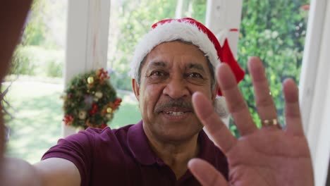 Porträt-Eines-Glücklichen-älteren-Mannes-Mit-Weihnachtsmütze,-Der-Während-Eines-Weihnachtsvideoanrufs-Mit-Der-Hand-Winkt