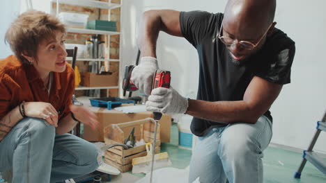 man stirring paint with drill and talking with wife about apartment renovation