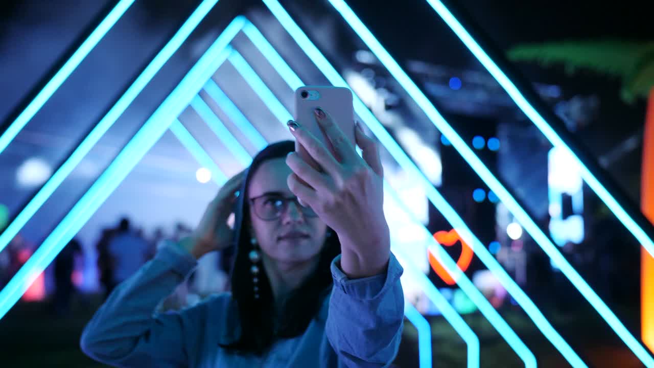 Woman on a neon party in the open air leads storis on smartphone.