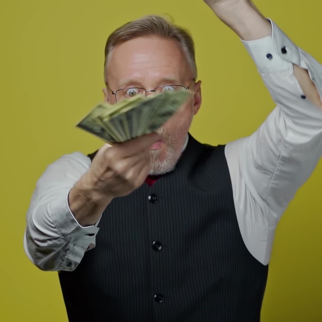 Good-looking joyful man with money on yellow background. Satisfied modern gray-bearded grandfather posing on camera with many dollar bills. Slow motion.