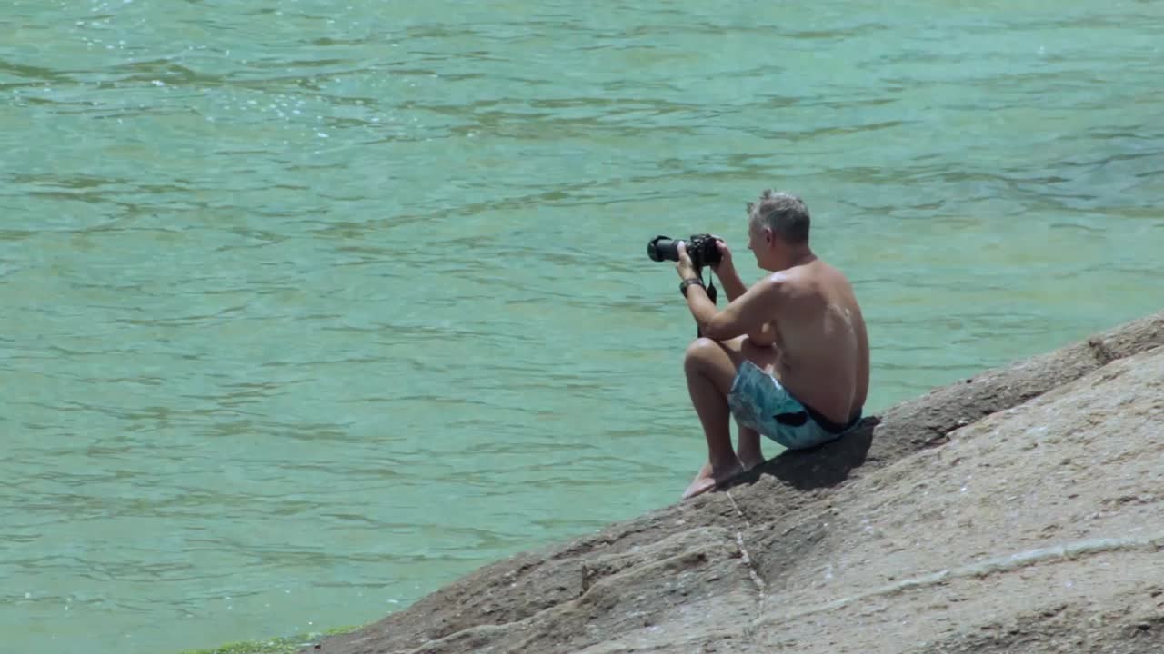 Old shirtless man photographing the ocean